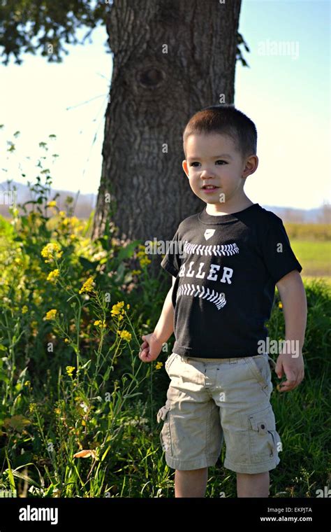 A Cute 3 Year Old Boy Standing By A Tree With Beautiful Yellow Flowers