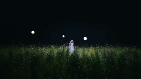 A Woman Standing In The Middle Of A Field At Night With Three Lights On
