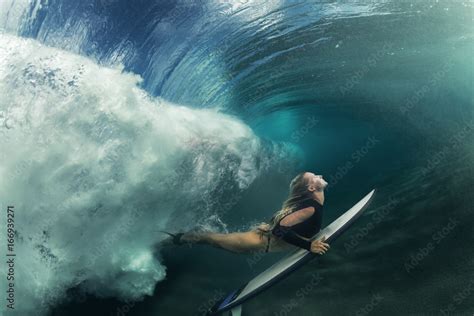 Poster Foto A Blonde Surfer Girl Underwater Doing Duck Dive Holding Surfing Board Left Behin