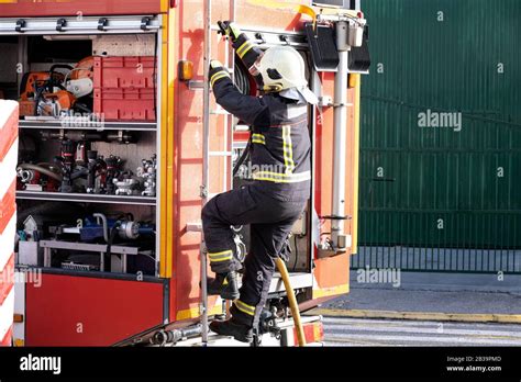 Fully Equipped Fireman Climbing The Ladder Of A Fire Truck Stock Photo