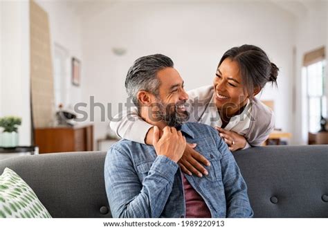 Smiling Ethnic Woman Hugging Her Husband On The Couch From Behind In