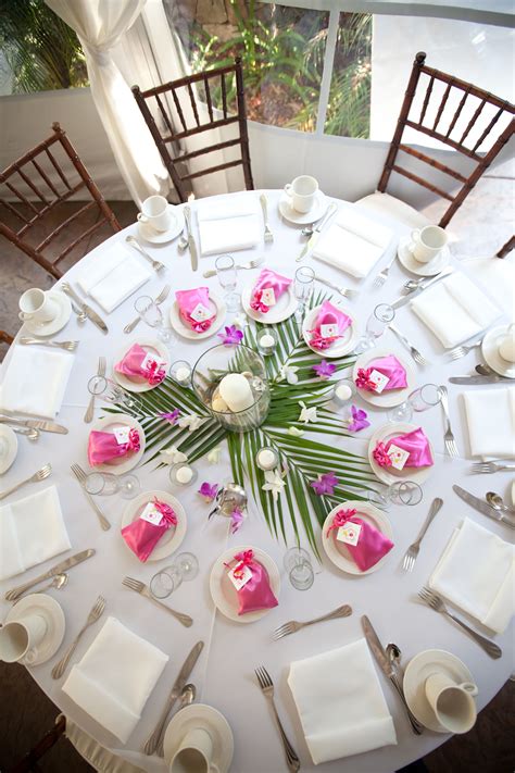 The Table Is Set With White Plates And Silverware Pink Napkins And Flowers