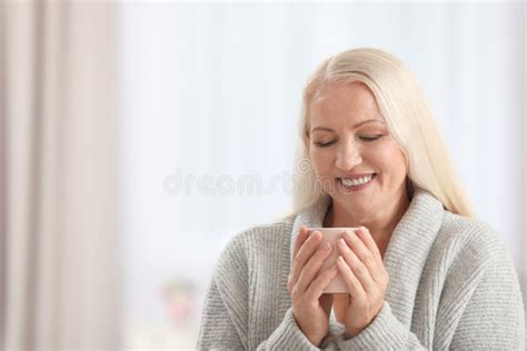 Portrait Of Beautiful Older Woman With Cup Of Tea Against Blurred