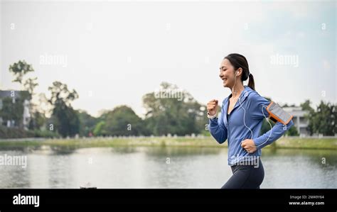 slim and active asian woman in sportswear listening to music while running or jogging along the