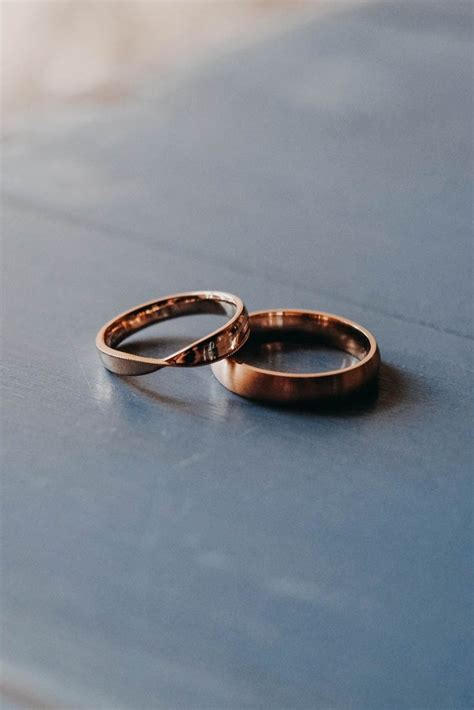 Two Gold Wedding Rings Sitting On Top Of A Blue Table Next To Each Other