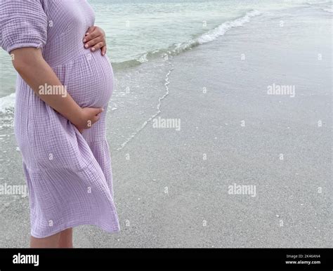Shot Of A Pregnant Woman Standing On The Beach With Her Hand Holding