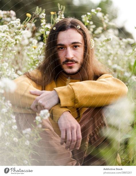 Young Man With Flowers In Long Hair Sitting In Field A Royalty Free