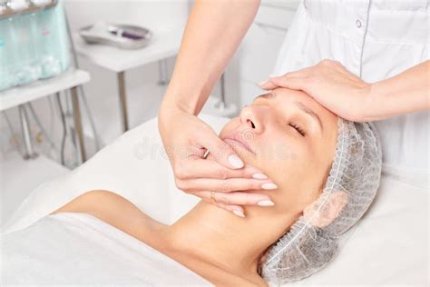 Beautician Massages Cream Mask Into Woman Face Skin For Rejuvenation Procedure In Beauty Salon