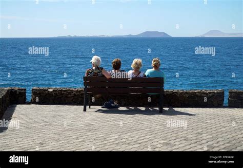 Four Older Ladies Sitting On Bench Looking At View Across Sea To