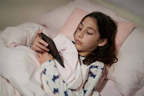 girl in pyjamas reading ebook on pad in her bed by stocksy contributor guille faingold