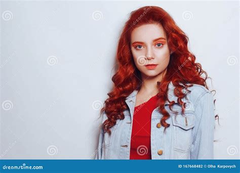 Portrait Of Beautiful Cheerful Redhead Girl With Flying Curly Hair Looking At Camera Over White