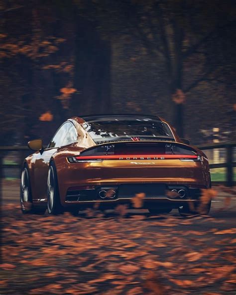 A Brown Sports Car Driving Down A Road Surrounded By Trees And Leaves