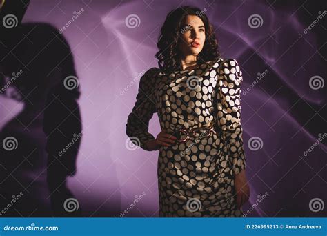 Beautiful Brunette Fashion Model In Polka Dot Dress Posing On A Lilac Background Shadow And