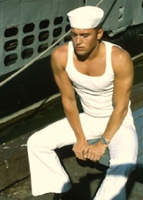 A Man In White Is Sitting On A Bench Near A Boat And Holding A Knife
