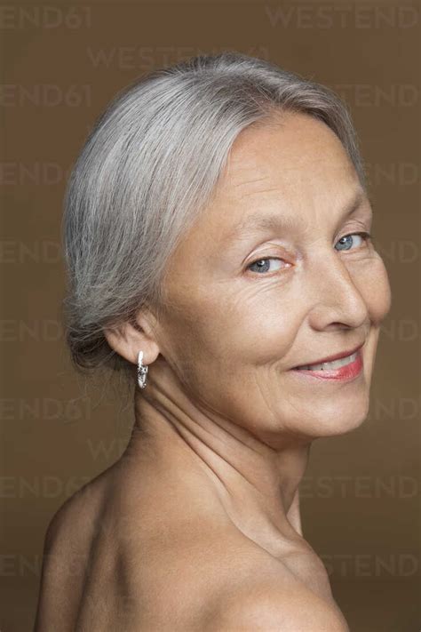 Portrait Of Naked Senior Woman With Grey Hair In Front Of Brown