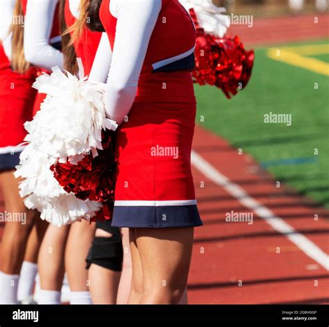 A High School Cheerleader Is Holding Her Pom Poms Behind Her Back While