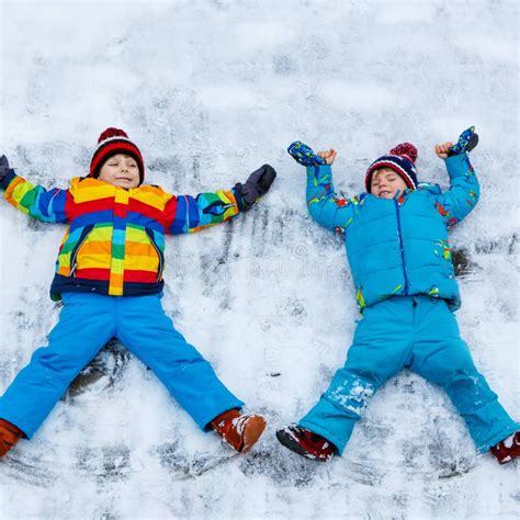 Two Little Kid Boys Making Snow Angel In Winter Outdoors Stock Photo