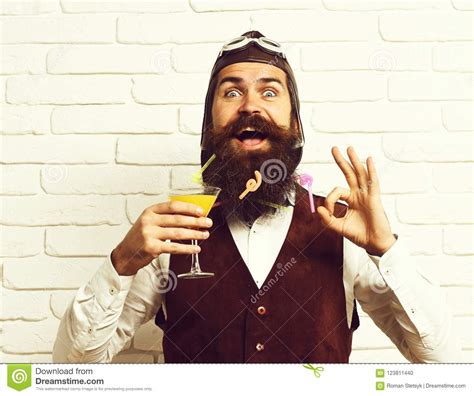 handsome bearded aviator man with long beard and mustache on happy face holding glass of