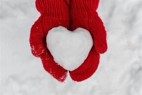 Close Up Of Two Hands In Red Mittens Holding Heart Shaped Snowball Stock Photo