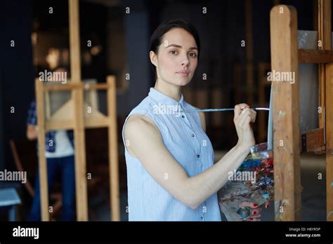 Attractive Female Artist With Palette And Brush Painting On Easel In School Of Arts Stock Photo