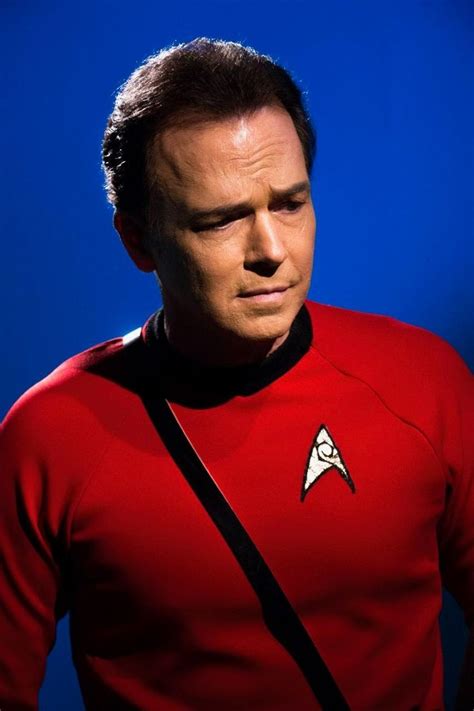 A Man In A Red Star Trek Uniform Looking At The Camera With His Hand On