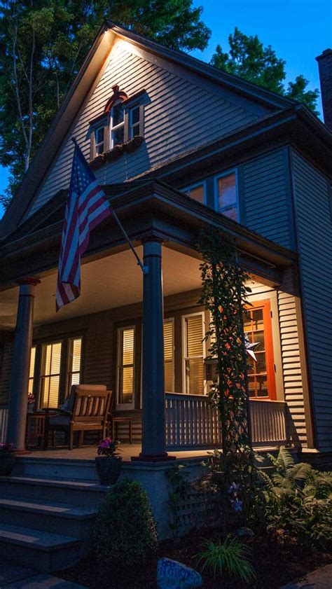 An American Flag Is Lit Up On The Front Porch Of A House At Night With