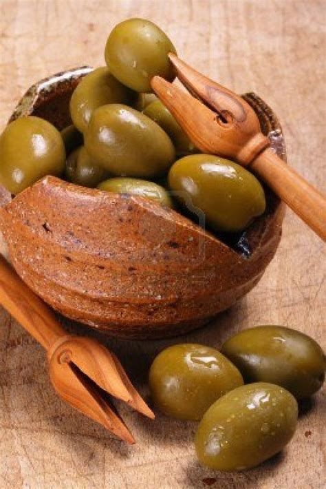 A Bowl Filled With Green Olives And Wooden Utensils