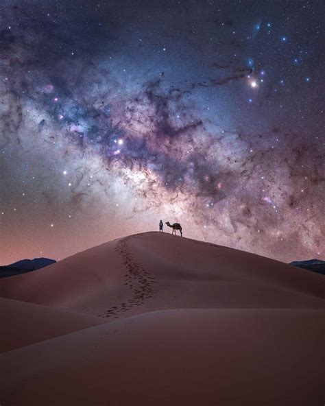 Two People Standing On Top Of A Sand Dune Under A Night Sky Filled With