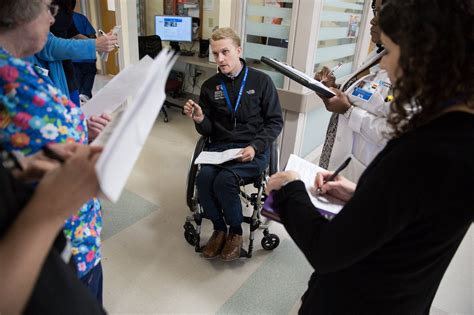 A Man In A Wheel Chair Talking To Two Women Who Are Holding Papers And