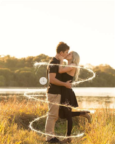 A Man And Woman Kissing In Front Of A Lake With Sparklers On The Grass