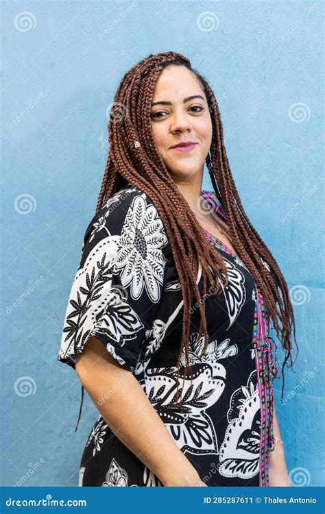 portrait of a beautiful woman with braids in her hair standing against a blue colored wall stock