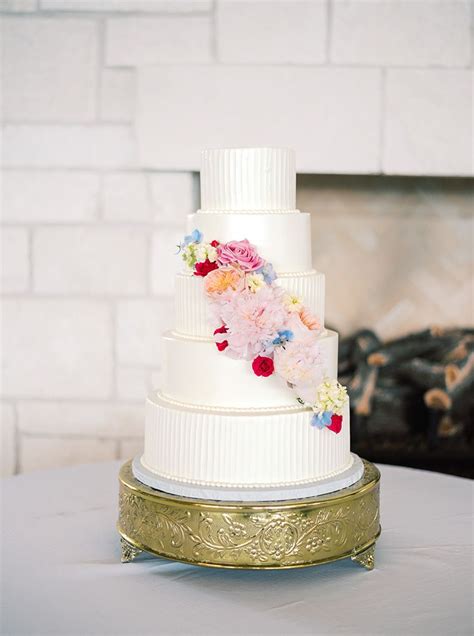 A White Wedding Cake With Flowers On It Sitting On Top Of A Round Table
