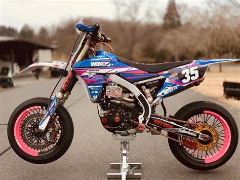 A Blue And Pink Dirt Bike Parked On Top Of A Metal Stand In The Street