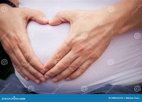 Husband Hugs His Pregnant Wife By The Stomach And Makes Fingers In The Shape Of A Heart Stock