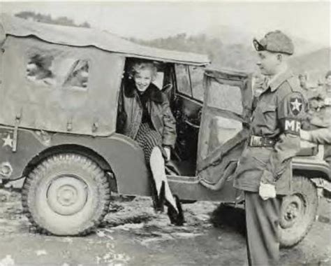 Marilyn Monroe Posing In A Jeep As An Unknown Mp Stands