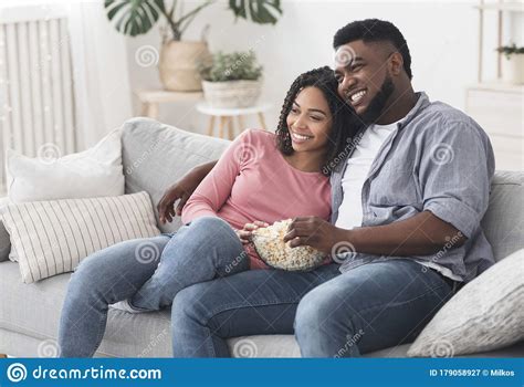 Relaxed African American Couple Watching Tv Sitting On Couch With