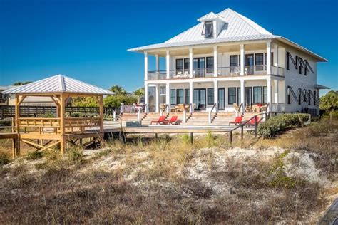Being raised on piling helps protect beach homes from flooding. piling house plans beach style exterior white metal roof double porch and deck pop red chairs ...