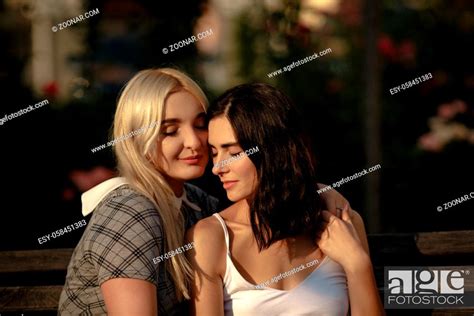 Blonde And Brunette Lesbians Holding Each Other Sitting On Bench