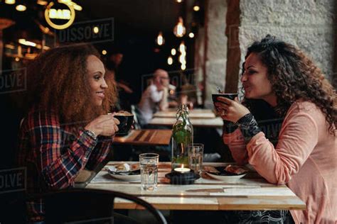 Side View Portrait Of Two Young Women Talking And Drinking Coffee In A