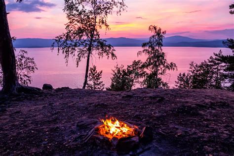 Campfire On The Shore Of A Picturesque Lake At Sunset Stock Photo