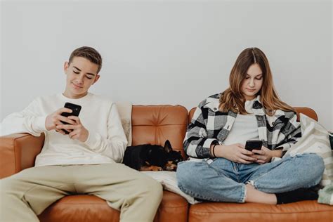 Young Man And Woman Sitting On Sofa Beside A Dog While Using Cellphones
