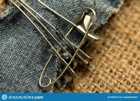 Safety Pins On A Strip Of Denim Against A Homespun Fabric With A Rough Texture Stock Photo