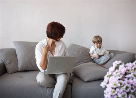 Mom And Son With Digital Gadgets Are Sitting On The Sofa In The Living