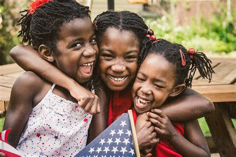 three african american girls in red white and blue usa flag outfits laughing by stocksy