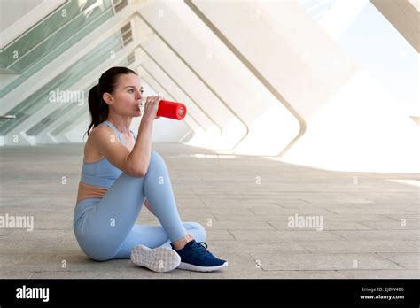Fit Sporty Woman Sitting Drinking Water From A Glass Bottle After