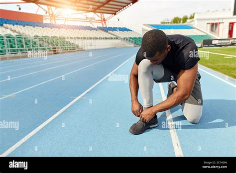 Sportsman Ties His Trainers Sitting On The Running Track Preparing