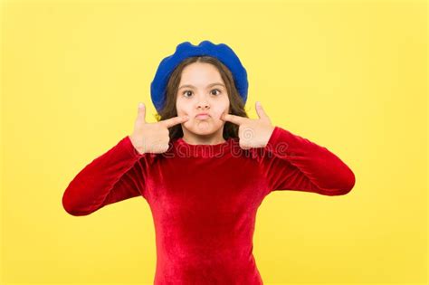 Funny Parisian Girl In French Beret Hat Making Faces And Pointing Finger On Cheeks Over Yellow