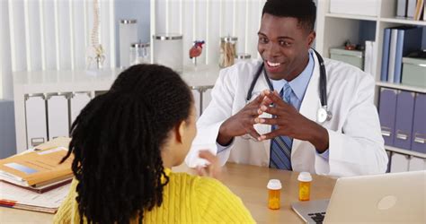 African American Woman Patient Speaking With Doctor At Office Desk