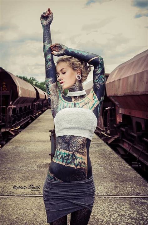 A Woman With Tattoos On Her Body Standing In Front Of Train Tracks And Holding Her Arms Up