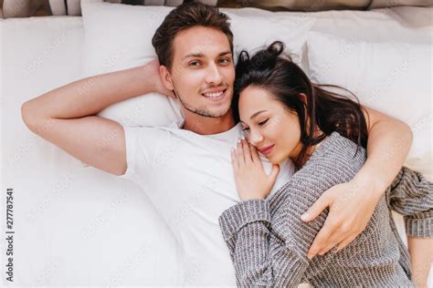 smiling man posing in bed with wife sleeping on his chest indoor overhead photo of chilling